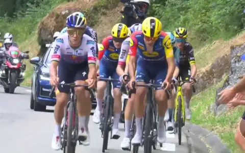 Radsportler im Peloton, darunter Cian Uijtdebroeks, kämpfen sich bergauf. Motorräder und ein Auto begleiten das Rennen.