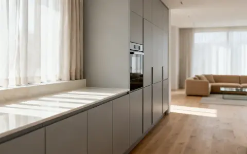 Cocina moderna con armarios grises y una encimera de mármol clara. La luz del sol entra por las cortinas blancas, iluminando el espacio.