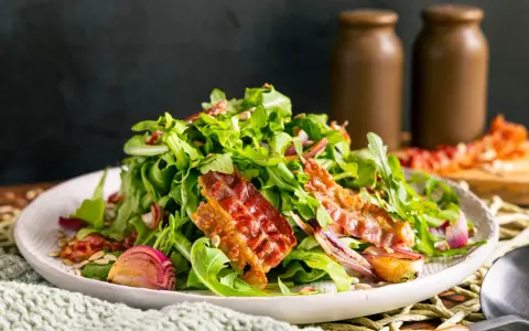 Salat mit Rucola, roten Zwiebeln und knusprigem Speck. Perfekte warme Beilagen zum Salat, die für zusätzlichen Geschmack sorgen.