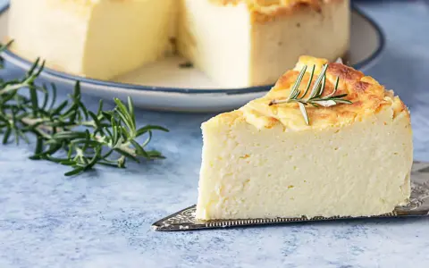 Una fetta di torta di ricotta soffice e dorata, guarnita con rosmarino, su un piatto da torta.