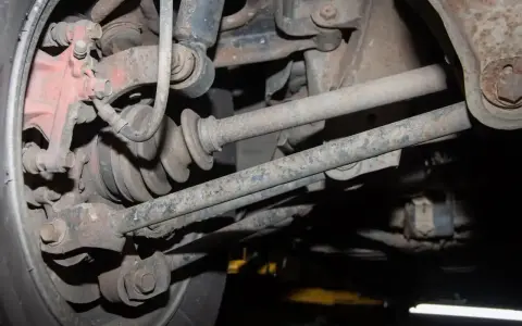 Widok od spodu na skorodowane elementy zawieszenia samochodu, w tym przegub napędowy i wahacze, tuż pod nadkolem.