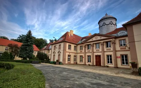 Pałac Maltzanów z charakterystyczną wieżą i czerwonym dachem, otoczony zielenią.