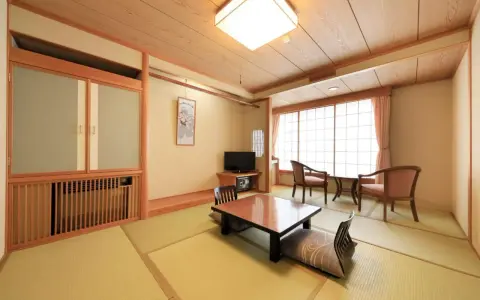 Wnętrze tradycyjnego ryokanu z tatami, niskim stolikiem i poduszkami do siedzenia.