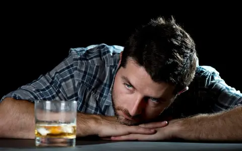 Mężczyzna zamyślony nad szklanką alkoholu. Może to być symbol walki z nałogiem, gdzie aplikacja "jestem wolny od" mogłaby pomóc.