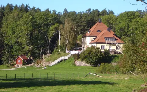 Gula huset vid grinda Stockholm, med röda stugor och grönskande träd.