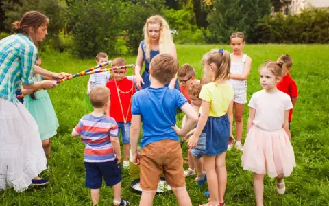 Des animateurs et des enfants jouent dehors dans l'herbe avec des cerceaux colorés.