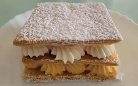 Delicioso milhojas de crema, con capas crujientes de hojaldre y rellenos de crema pastelera y nata montada, espolvoreado con azúcar glas.