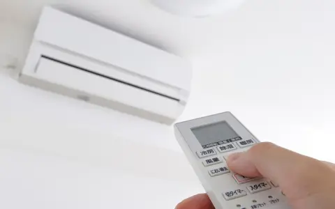 Mano ajustando el **timer on aire acondicionado** con el control remoto. El aire acondicionado blanco está montado en la pared.