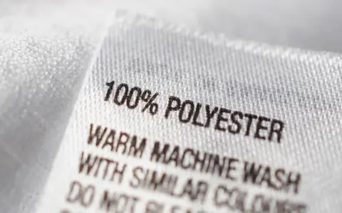 Etikett zeigt "100% POLYESTER". Dieser Stoff ist pflegeleicht und ideal für Kleidung, die oft gewaschen wird.