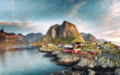 Röda fiskestugor vid en vik, med dramatiska berg i bakgrunden. En idyllisk vy som visar var ligger Lofoten.