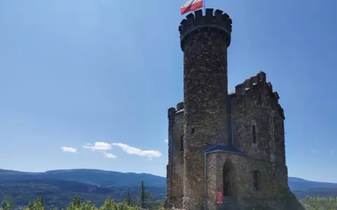 Kamienny zamek henryka na wzgórzu, z polską flagą na wieży, góruje nad zielonymi lasami i błękitnymi górami.