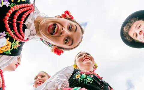 Uśmiechnięci młodzi ludzie w barwnych strojach ludowych, żywa ludowa twórczość artystyczna.
