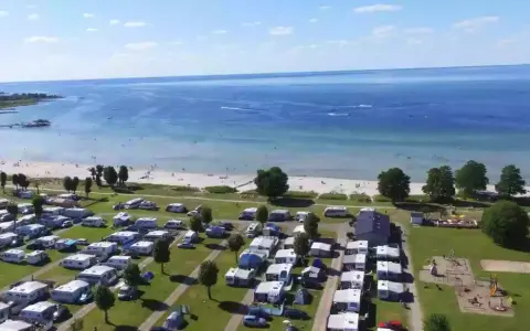 En stor campingplats vid havet nära Kalmar. Husvagnar och husbilar står uppradade på gräsmattor, med en strand och brygga i bakgrunden.