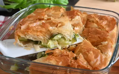 Una fetta di torta salata con zucchine, con croccante pasta sfoglia dorata e ripieno filante.