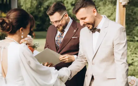 Uroczystość ślubna: panna młoda w białej sukni, pan młody w jasnym garniturze i urzędnik. To piękny ślub humanistyczny, a nie tylko cywilny.