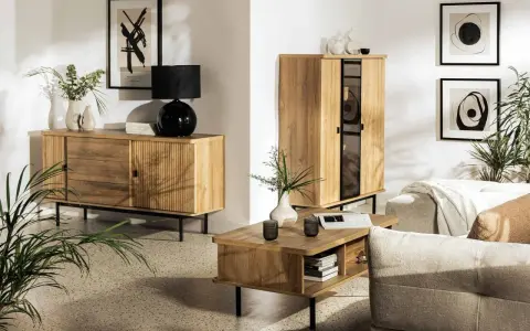 Drewniane meble i subtelne dodatki tworzą przytulną atmosferę w stylu hygge. Wazon z gałązkami i czarna lampa dodają elegancji.