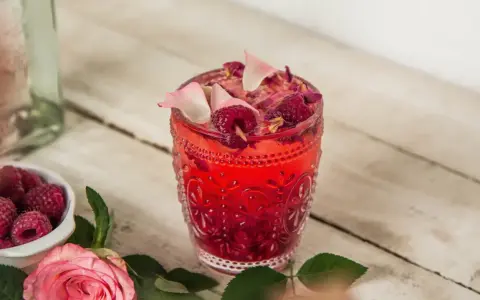 Orzeźwiający drink z malinami, ozdobiony płatkami róż i świeżymi malinami. Idealny na letnie popołudnie.