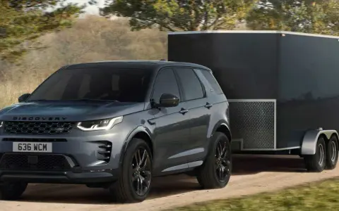 Szary Land Rover Discovery Sport z przyczepą o masie 2000 kg jedzie po leśnej drodze.
