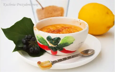 Słodka, karmelizowana crema catalana w ozdobnej miseczce, obok cytryna i jagody.