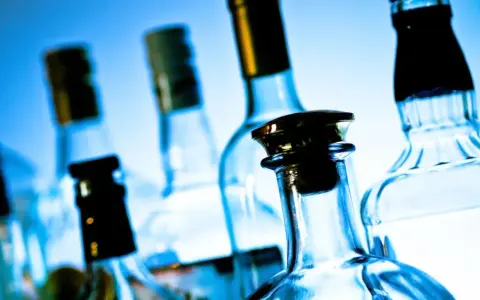 Kilka szklanych butelek alkoholu na niebieskim tle.