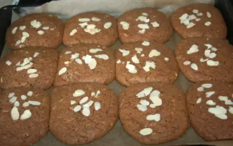 Douze biscuits faits maison, parfaits pour une recette speculoos, garnis d'amandes effilées sur une plaque de cuisson.
