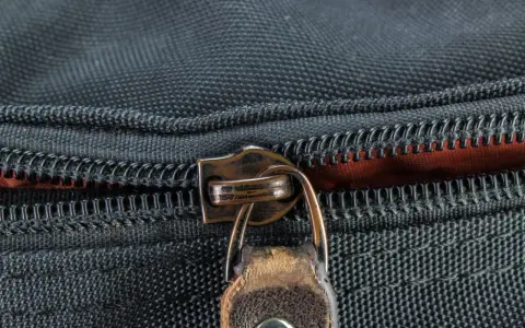 Nahaufnahme eines Reißverschlusses an einer schwarzen Tasche. Der Schieber ist aus Metall und leicht abgenutzt, was auf die Notwendigkeit hinweist, den Reißverschluss zu reparieren.