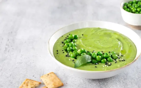 Cremoso hummus di piselli guarnito con piselli freschi, basilico e semi di sesamo, servito con cracker croccanti.