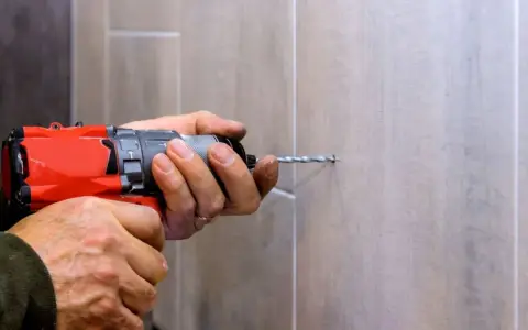Man usa una broca para azulejo con un taladro para hacer un agujero en una pared de azulejos.