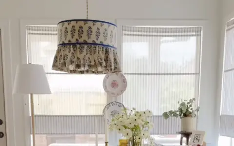 Un abat-jour suspendu avec un motif floral bleu et des volants, une excellente idée déco abat jour. Des assiettes décoratives et des fleurs complètent la scène.
