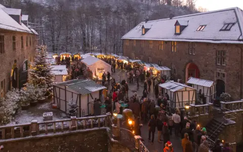 Schneebedeckter Weihnachtsmarkt in einer Burg, ein echter Geheimtipp NRW. Besucher schlendern zwischen festlich beleuchteten Buden.