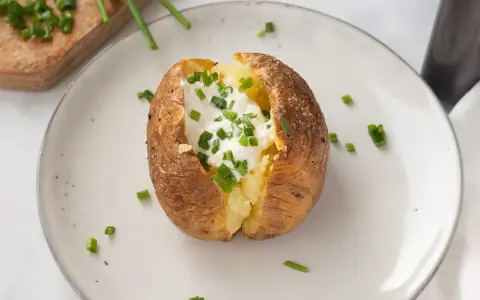 Patatas asadas en freidora de aire, crujientes por fuera, tiernas por dentro, coronadas con crema agria y cebollino fresco.