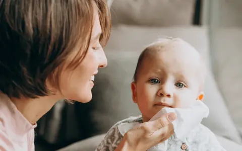 Mama delikatnie wyciera buzię dziecka, które ma żółty katar.
