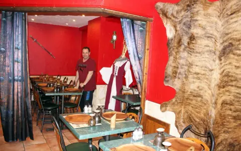 Un homme se tient dans un restaurant moyen âge décoré d'une peau d'ours et d'une épée.