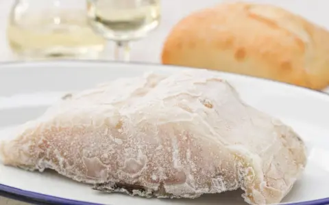 Un trozo de pescado en blanco, escarchado, listo para cocinar. Acompañado de pan y vino blanco.