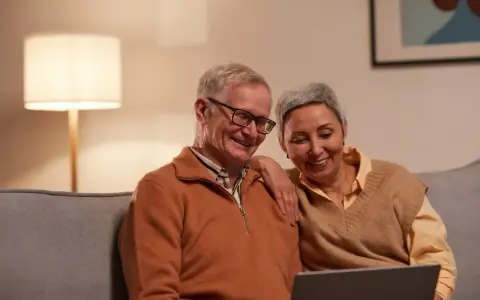 Uśmiechnięta para seniorów przegląda coś na laptopie. Zastanawiają się, czy zwolnienia lekarskie mają wpływ na wysokość emerytury.