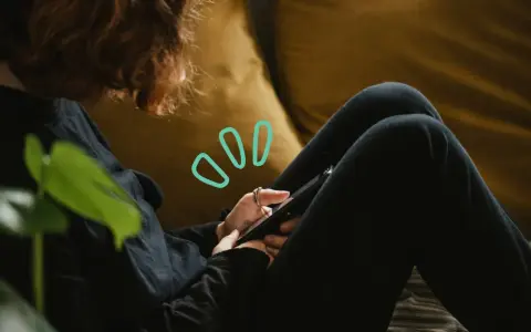 Une personne aux cheveux roux utilise son smartphone, symbolisant quelles peuvent être les principales conséquences de la cyberdépendance : isolement, anxiété, perte de temps.