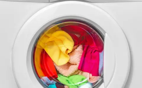 Bunte Wäsche, darunter ein gelber und ein grüner Schwamm, wartet in der Waschmaschine auf das schwamm waschen.