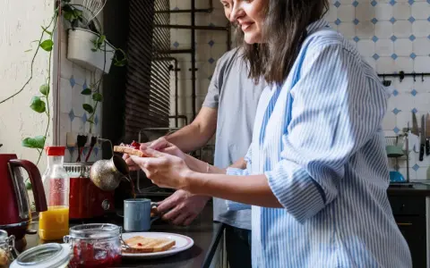 Pareja preparando el desayuno, tostadas con mermelada y café. Un momento de "bonjour" en francés para empezar el día.