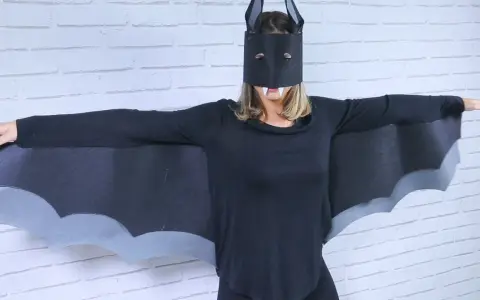 Persona con un disfraz murciélago casero, alas negras y máscara con colmillos.