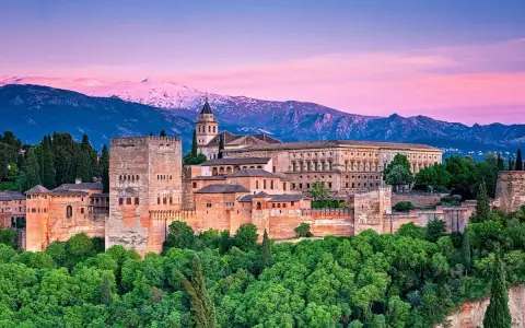 Alhambra w Granadzie na tle ośnieżonych gór i różowego nieba o zachodzie słońca.