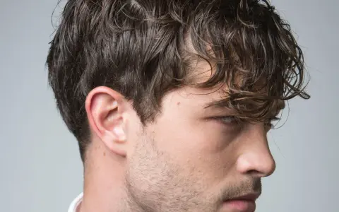 Perfil de hombre con cabello castaño ondulado y barba incipiente. Su corte de pelo es un rapado al 3 en los laterales.