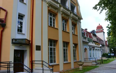 Sanatorium Jan Kazimierz w Dusznikach-Zdroju, z charakterystyczną żółto-kremową fasadą i czerwonym dachem, otoczone zielenią.