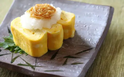 Delikatny omlet tamago, zwinięty w rolki, podany z tartą rzodkwią i grzybami enoki na talerzu z bambusowym wzorem.