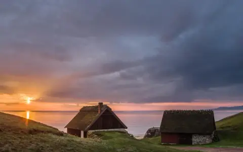 Två gamla hus med halmtak vid havet i Skåne Tranås. Solnedgången färgar himlen orange och lila.