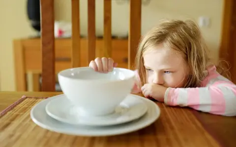 Smutna dziewczynka przy pustej misce. Zastanawia się, co do jedzenia przy wymiotach u dziecka, by jej pomóc.