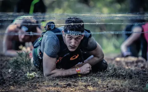 En deltagare i ett ocr sport-lopp kryper under taggtråd.
