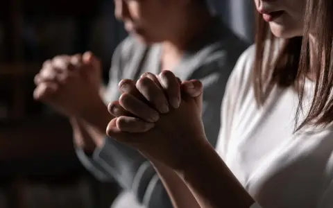 Two women pray, hands clasped. One's face is blurred, the other's lips are visible. This scene evokes the devotion of a deaconess in the bible.