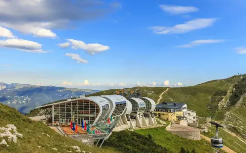 Moderne Seilbahnstation am Monte Baldo mit Panoramablick auf die Berge. Eine Gondel fährt den Hang hinauf.
