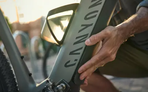 En hand justerar en elcykel. Solen skiner genom ett fönster på cykelns ram.