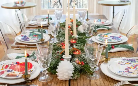 Une table dressée pour les fêtes, avec des assiettes décorées, des bougies allumées et une guirlande de sapin, évoquant la magie des arts de la table.